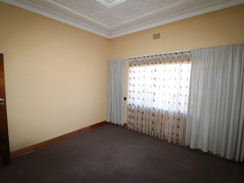 An empty bedroom featuring a decorative ceiling rose, timber door, and timber skirting boards, providing a neutral canvas for interior design.