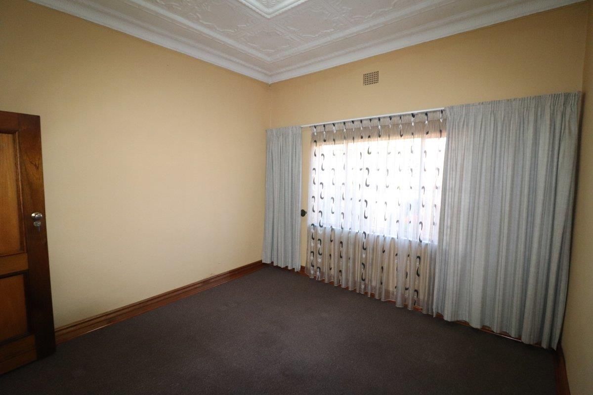 An empty bedroom featuring a decorative ceiling rose, timber door, and timber skirting boards, providing a neutral canvas for interior design.