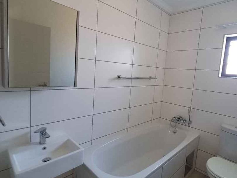 A clean, functional bathroom featuring white wall tiles, a bathtub, a wall-mounted basin, and a mirrored medicine cabinet.