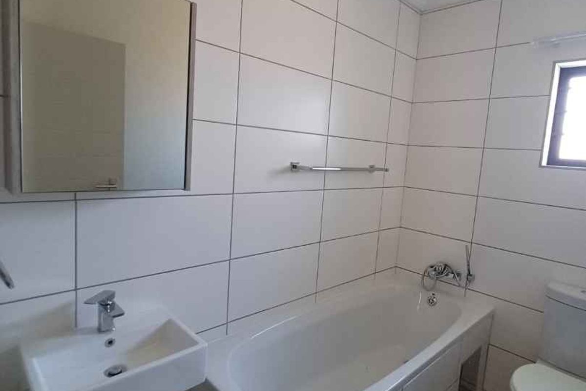A clean, functional bathroom featuring white wall tiles, a bathtub, a wall-mounted basin, and a mirrored medicine cabinet.