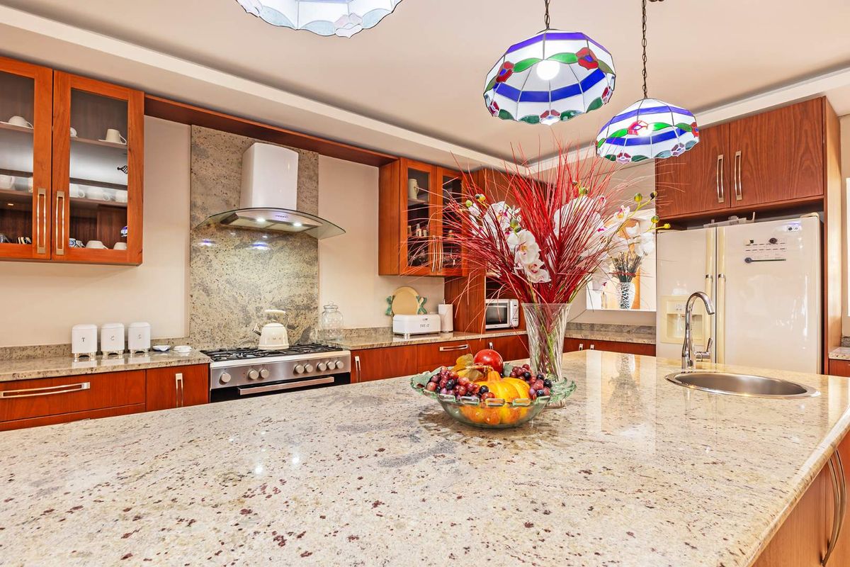 A well-appointed kitchen featuring granite countertops, a central island with an integrated sink, gas cooktop, and warm-toned wooden cabinetry.