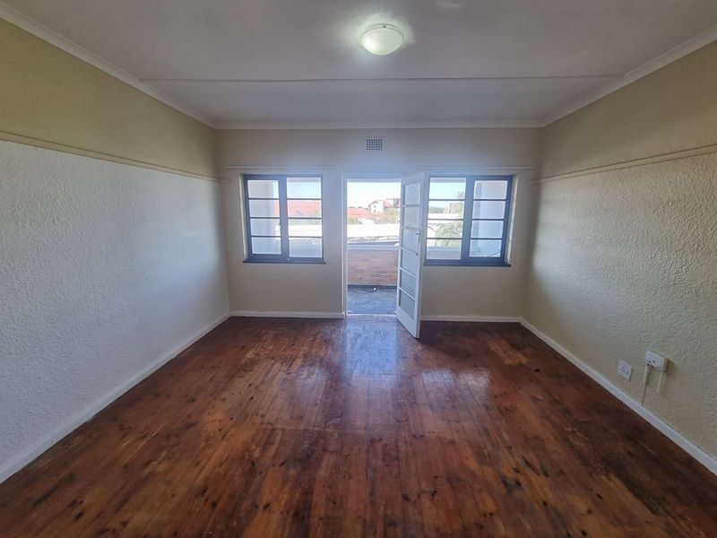 An empty bedroom featuring original timber flooring, picture rails, and direct access to a private balcony through a glass-paneled door.