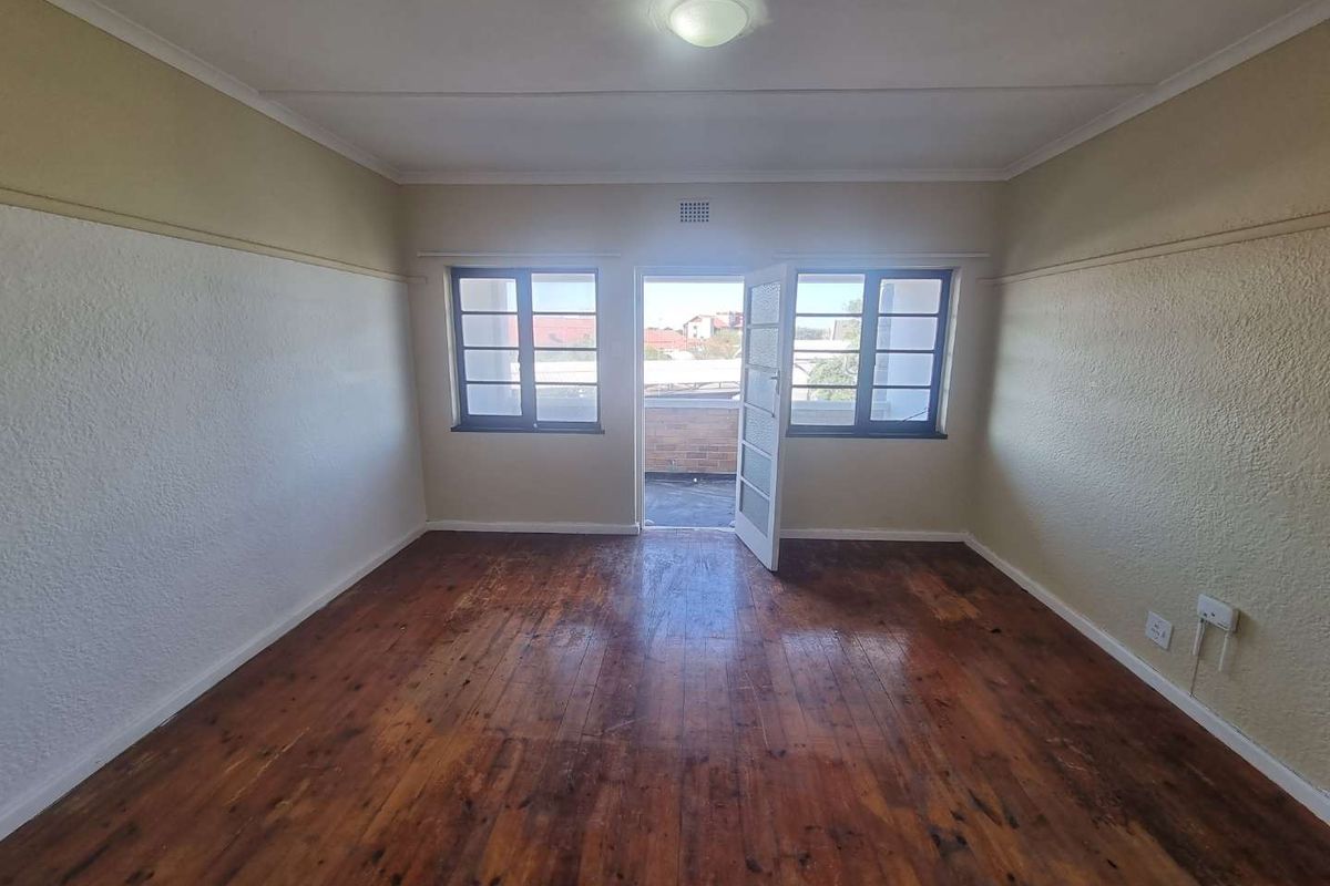 An empty bedroom featuring original timber flooring, picture rails, and direct access to a private balcony through a glass-paneled door.