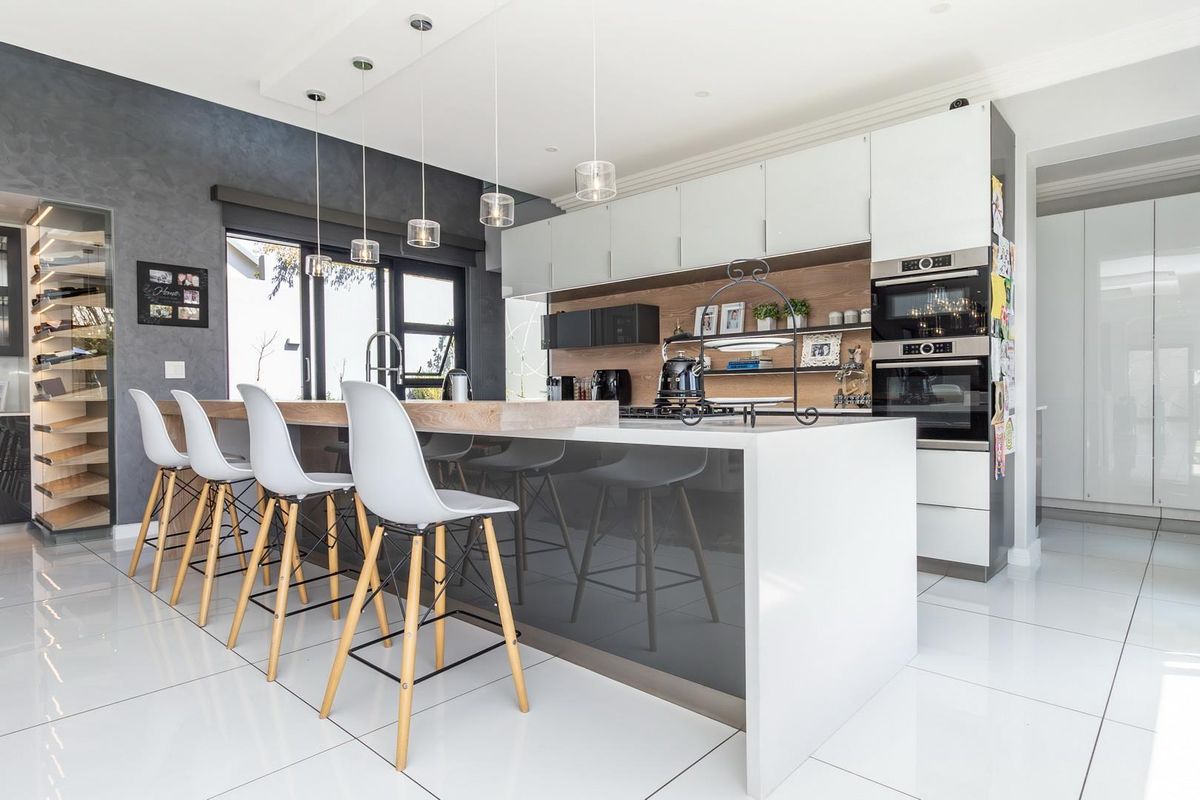 Modern kitchen featuring a large central island with breakfast bar, integrated double ovens, sleek cabinetry, and high-gloss floor tiles.