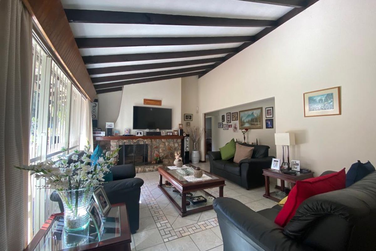 Spacious living room featuring a vaulted ceiling with exposed timber beams, a stone-clad fireplace, and tiled flooring with decorative inlay.