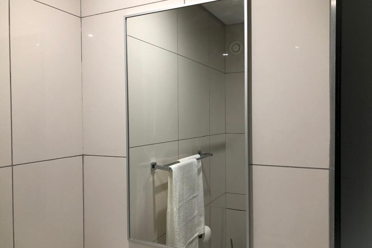 A clean, modern bathroom featuring large-format neutral wall tiles, a sleek rectangular mirror, and a chrome towel rail.