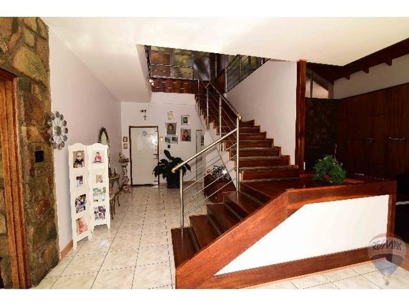 Spacious entrance hall featuring a prominent wooden staircase with stainless steel balustrades and natural stone wall accents.