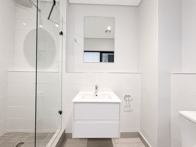 Modern bathroom featuring a wall-mounted vanity, glass shower enclosure with rain shower head, and clean white tiling throughout.