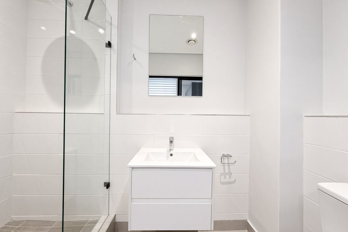 Modern bathroom featuring a wall-mounted vanity, glass shower enclosure with rain shower head, and clean white tiling throughout.