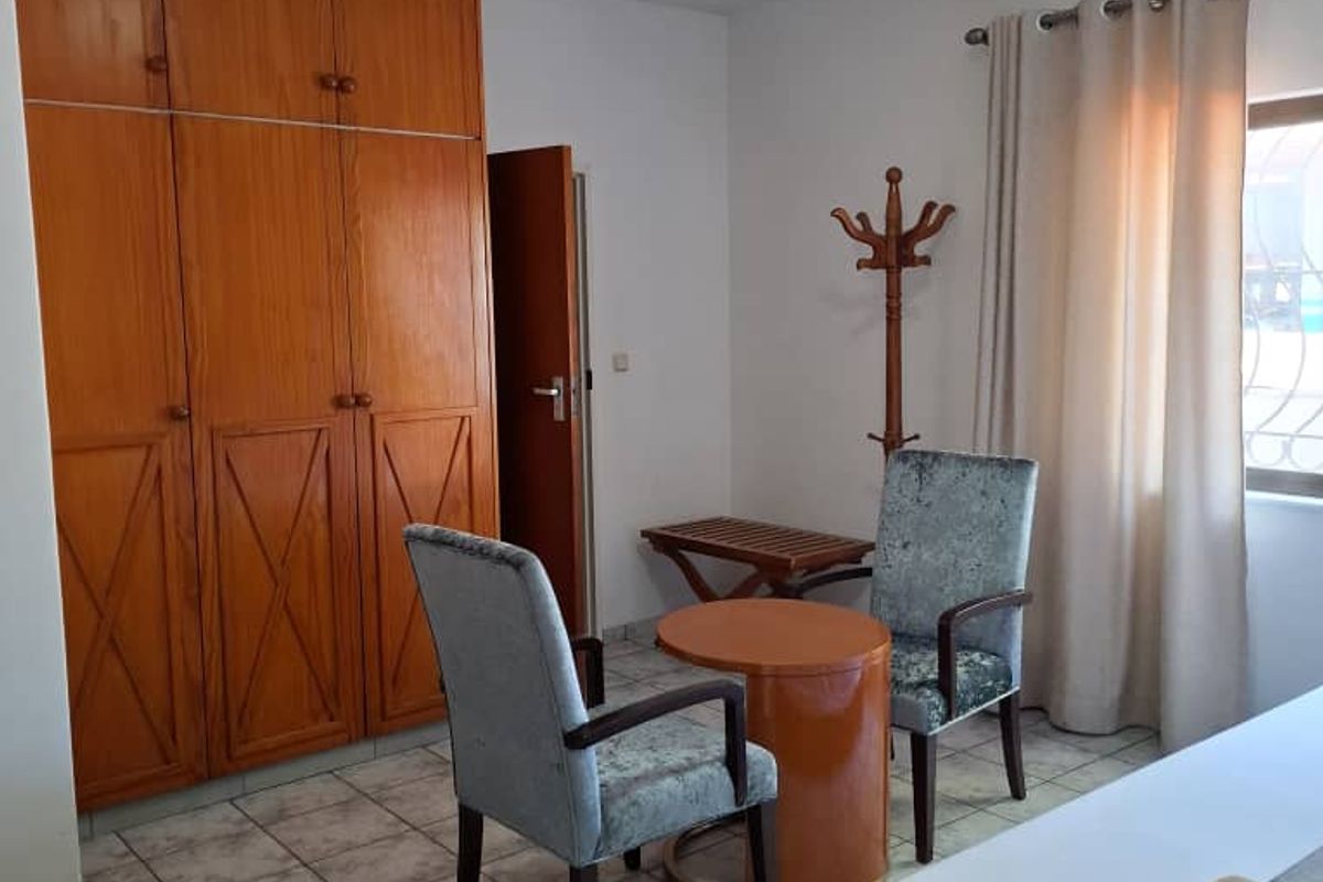 A hotel bedroom featuring built-in wooden wardrobes, tiled flooring, and a window with curtain treatments.
