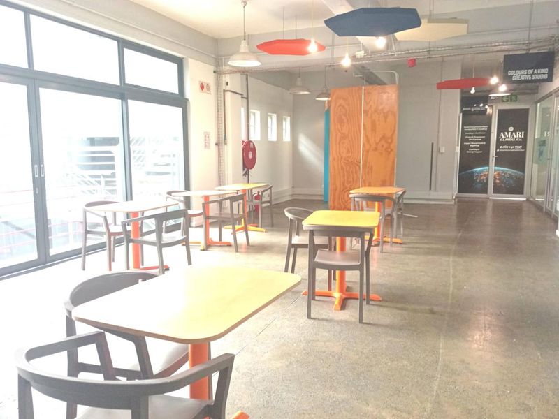 Open-plan office space featuring polished concrete floors, exposed industrial ceilings with acoustic panels, and large glass sliding doors providing ample natural light.