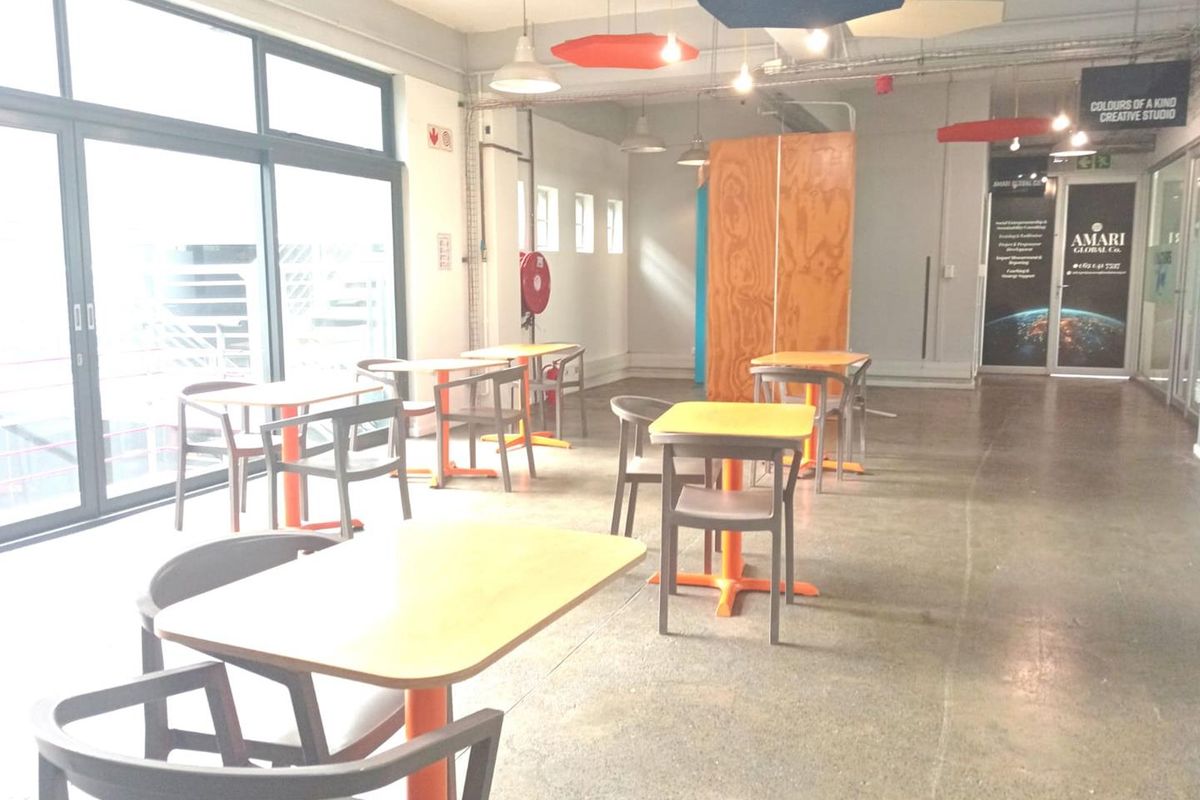 Open-plan office space featuring polished concrete floors, exposed industrial ceilings with acoustic panels, and large glass sliding doors providing ample natural light.