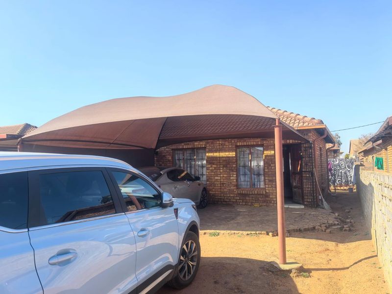 Front exterior view of a face brick house featuring a shade cloth carport and paved driveway area.