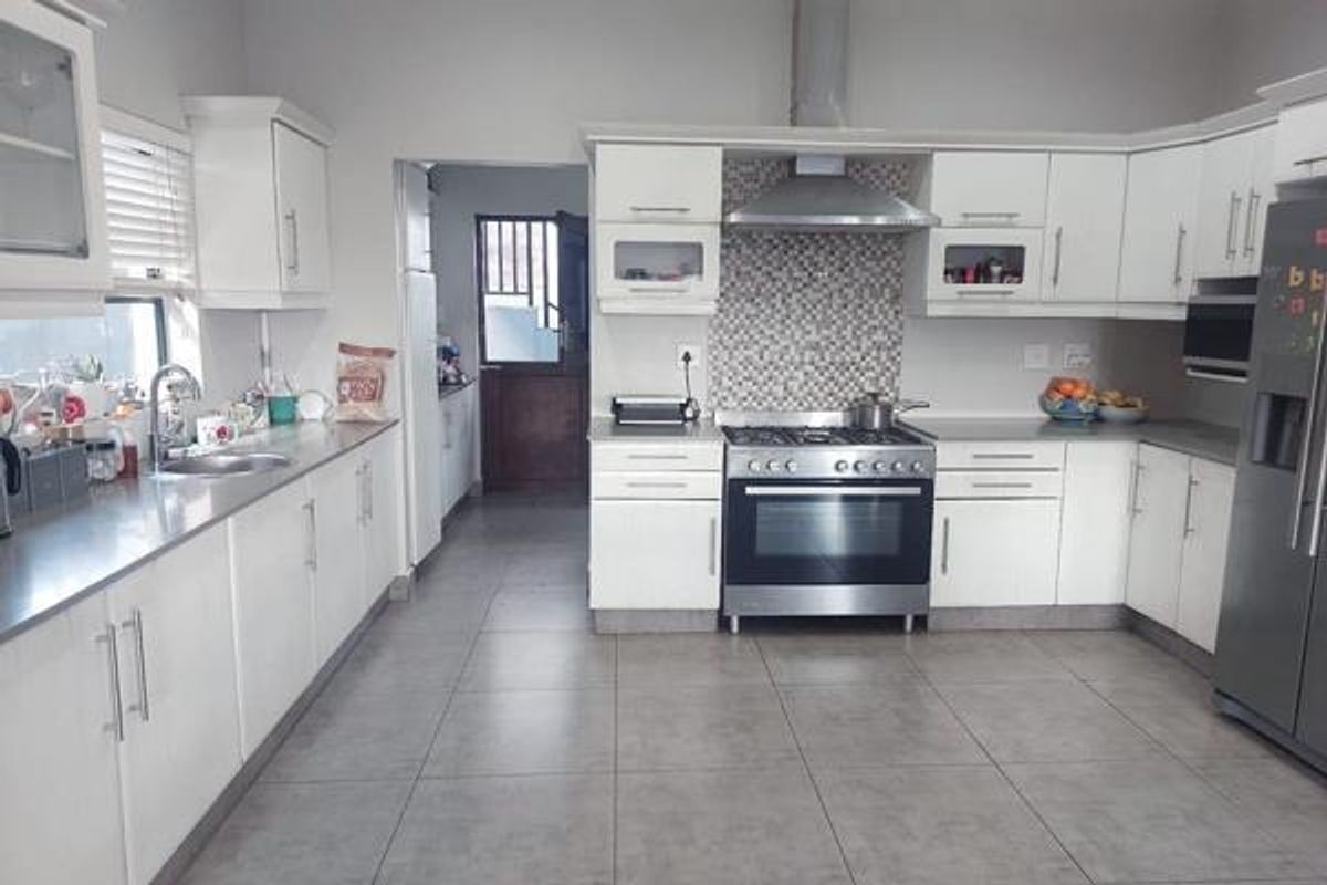A functional kitchen featuring white cabinetry, stainless steel appliances, a gas hob with extractor fan, and a mosaic tile backsplash.