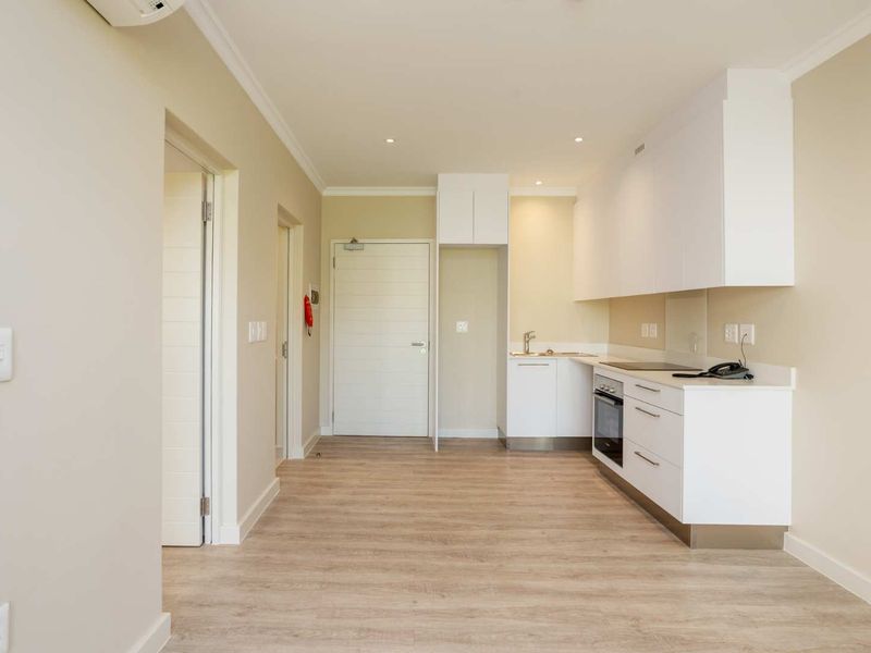 A clean, modern kitchen featuring white cabinetry, integrated appliances, laminate flooring, and recessed lighting in an open-plan apartment layout.