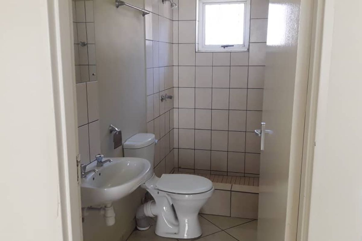 A functional bathroom featuring a pedestal basin, toilet, and a tiled shower enclosure with a window for natural ventilation.