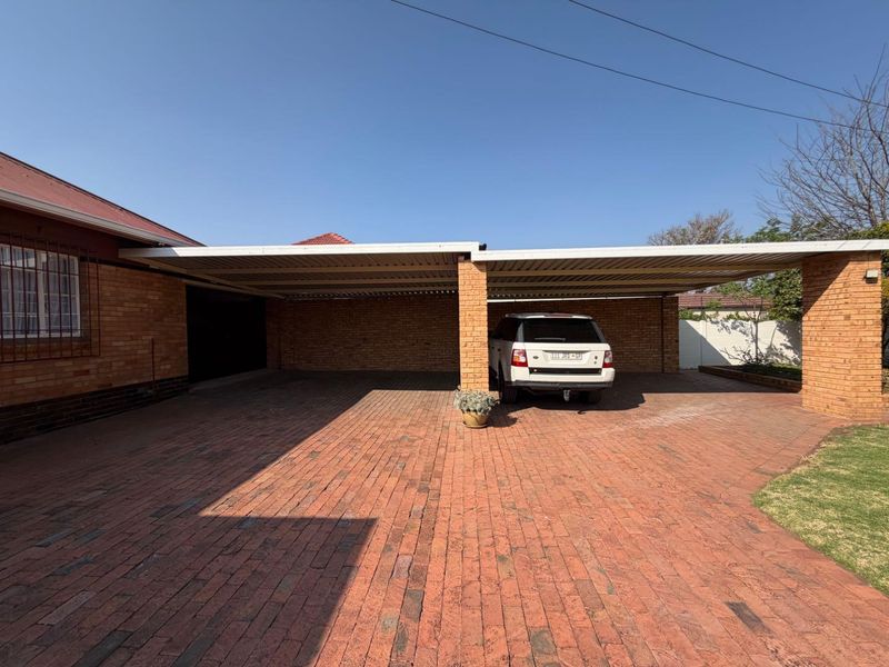 A spacious covered carport featuring durable facebrick pillars and extensive brick paving, providing ample sheltered parking space.