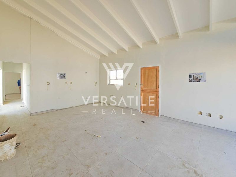 An empty, unfinished living area featuring exposed beam ceilings, tiled flooring, and a timber door, currently undergoing renovation or awaiting final finishes.