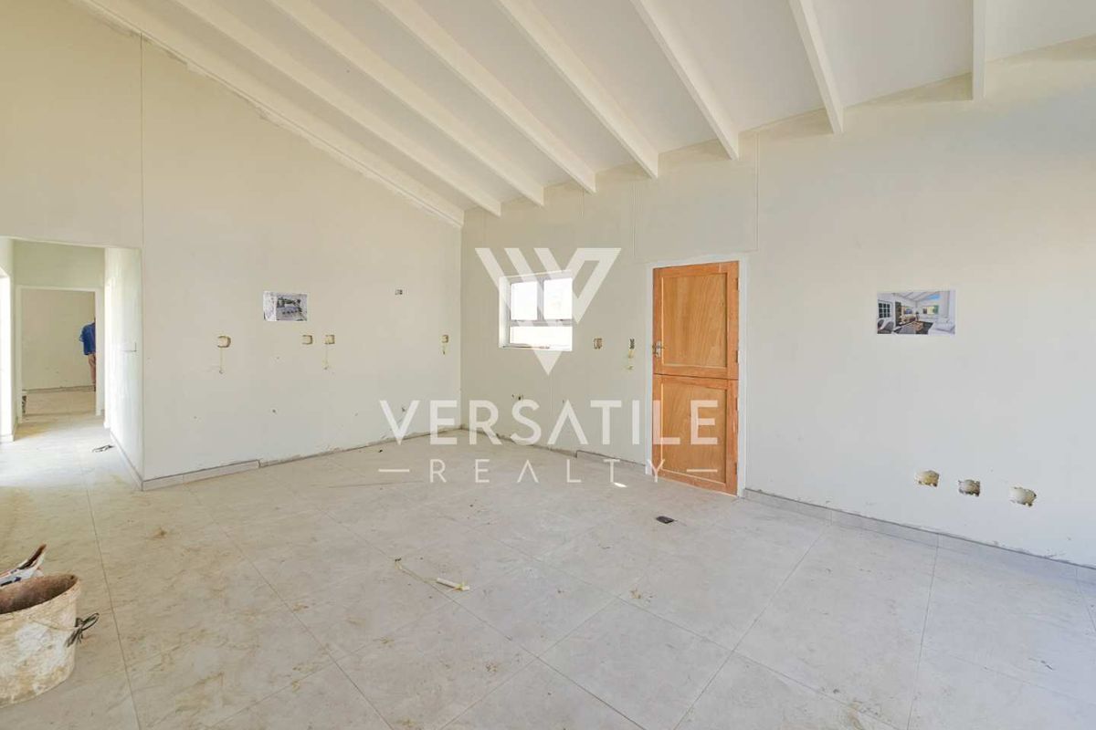 An empty, unfinished living area featuring exposed beam ceilings, tiled flooring, and a timber door, currently undergoing renovation or awaiting final finishes.
