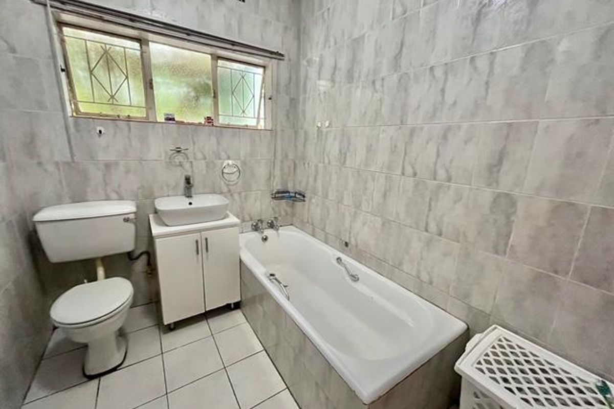 A functional bathroom featuring a standard bathtub, vanity basin, and toilet, finished with full-height wall tiling and tiled flooring.
