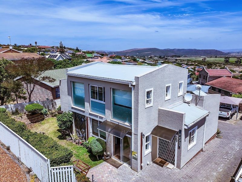 Aerial view of a two-story residential property featuring a metal roof, paved driveway, and surrounding garden area with scenic landscape views.