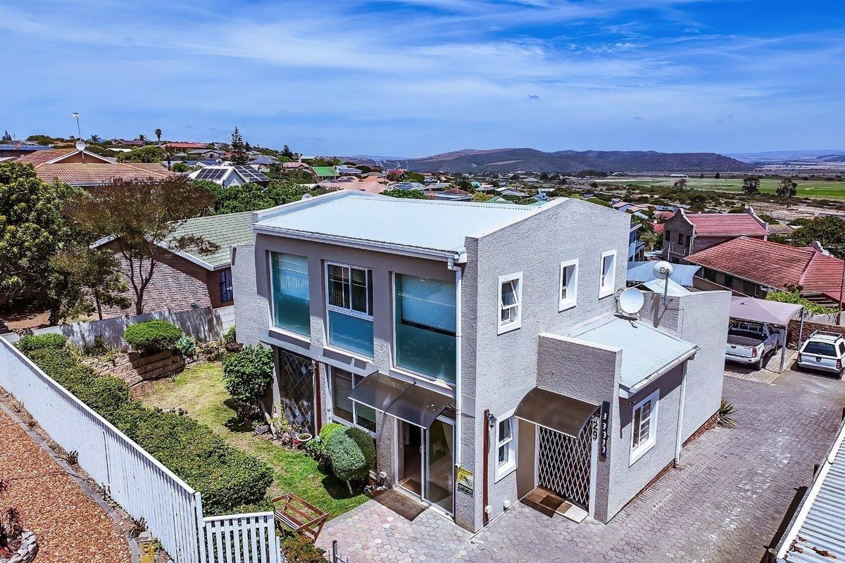 Aerial view of a two-story residential property featuring a metal roof, paved driveway, and surrounding garden area with scenic landscape views.