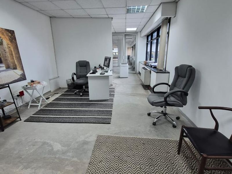 A functional office space featuring a suspended ceiling, recessed lighting, large windows, and exposed concrete flooring.