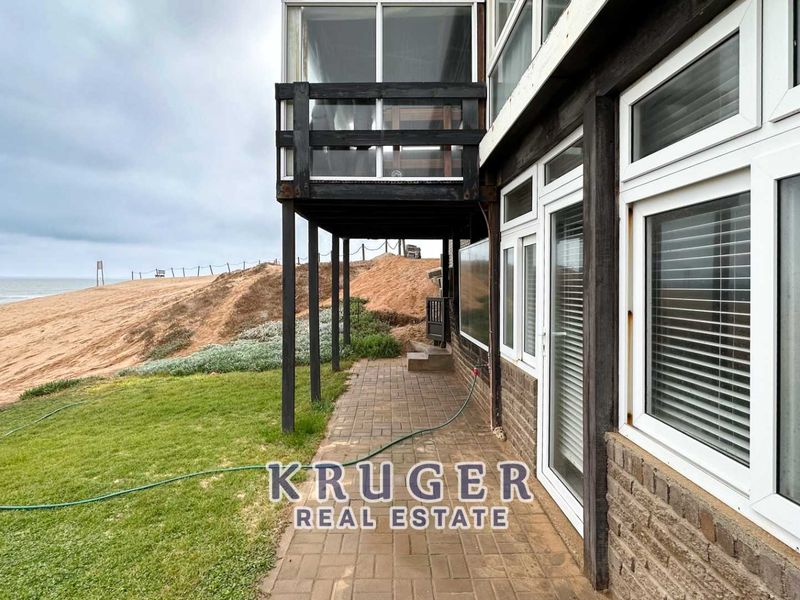 Rear exterior view of the townhouse featuring a paved patio, raised timber deck, and direct access to the coastal landscape.