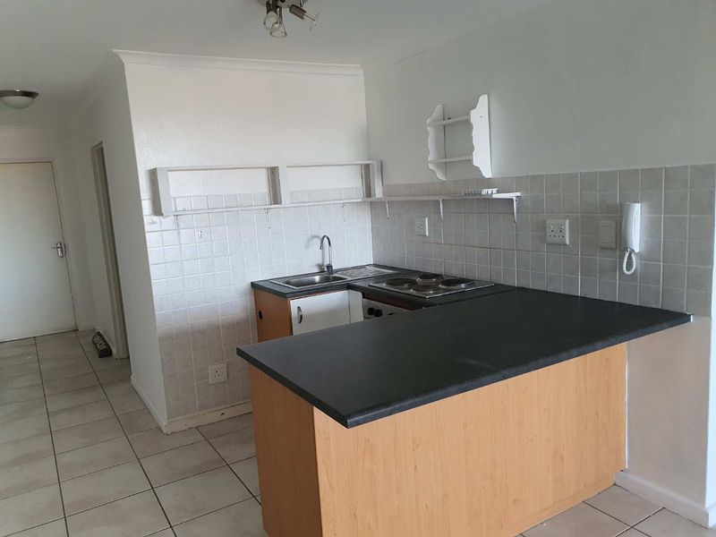 A compact, functional kitchen featuring built-in cabinetry, a dark laminate countertop, an electric hob, and neutral ceramic wall and floor tiling.