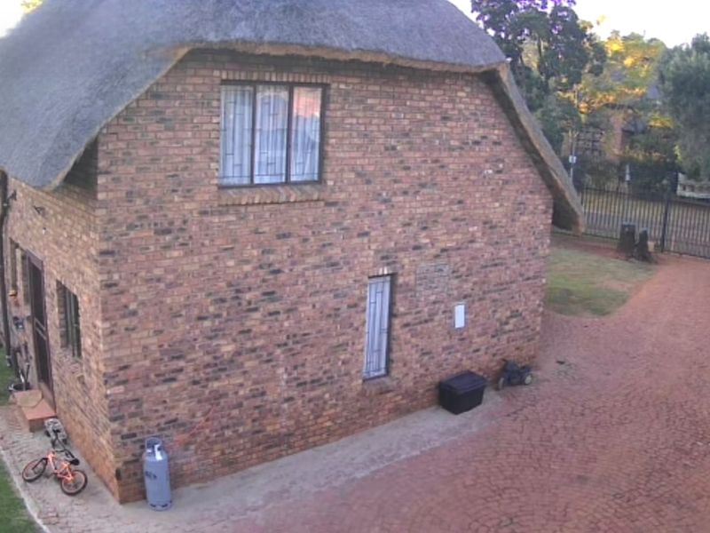 A side view of a face brick house featuring a traditional thatch roof, security bars on windows, and a paved driveway area.