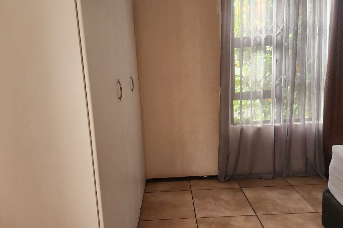 A bedroom featuring tiled flooring, a built-in wardrobe, and a window with security gate, offering a functional space with potential for cosmetic updates.