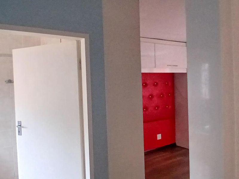 A view from a hallway looking into a bathroom and a bedroom featuring built-in cabinetry and contrasting wall finishes.