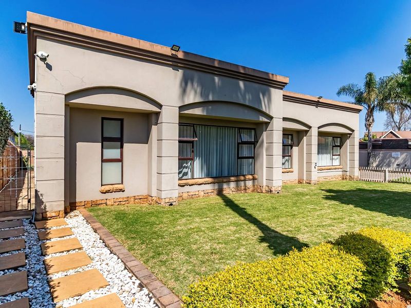 Rear view of the property featuring a well-maintained lawn, stone-clad base, plastered facade, and paved walkway leading to a secure side gate.