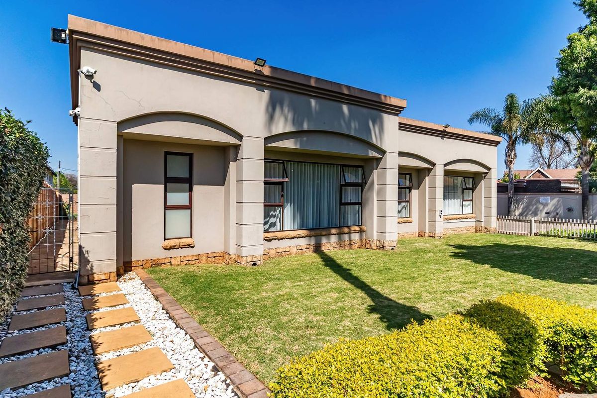 Rear view of the property featuring a well-maintained lawn, stone-clad base, plastered facade, and paved walkway leading to a secure side gate.