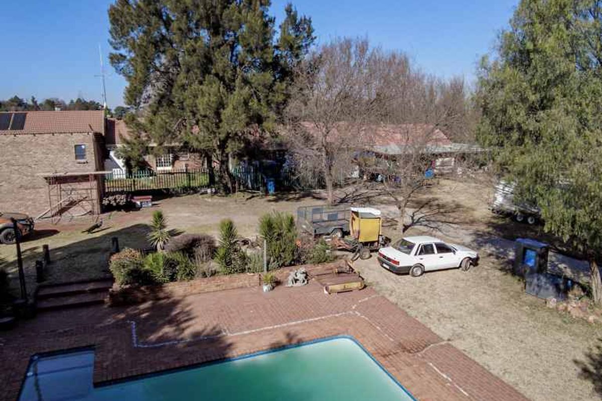 Aerial view of a farm property featuring a swimming pool, brick patio area, and surrounding garden space with existing outbuildings.