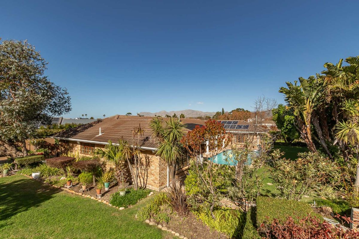 Aerial view of the property featuring a brick exterior, tiled roof, solar panels, and a private swimming pool set within a landscaped garden.