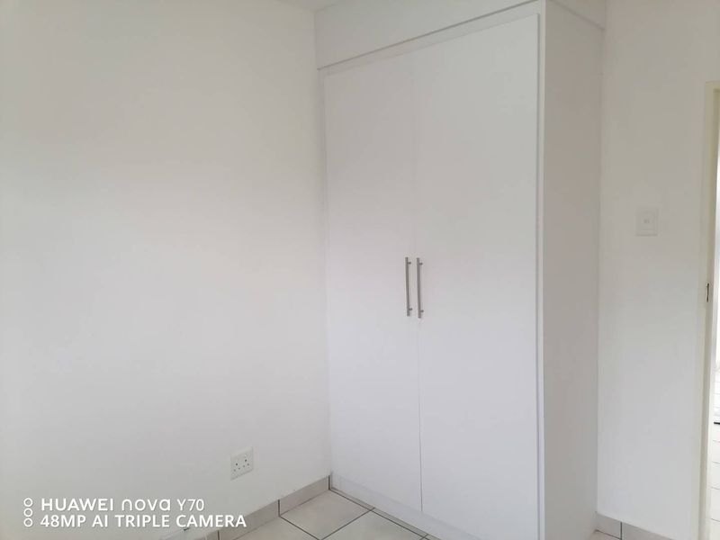 A clean, empty bedroom featuring a white built-in wardrobe and neutral tiled flooring, providing a blank canvas for personalization.