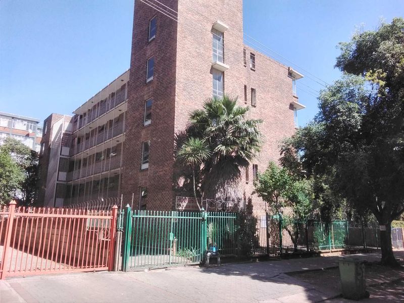 Exterior view of a multi-story brick apartment building featuring security fencing, gated access, and private balconies.