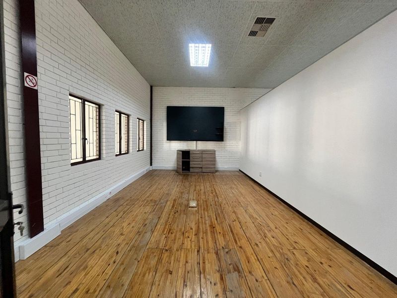 A spacious office area featuring timber flooring, exposed brick walls, and integrated ceiling lighting, providing a functional workspace with a neutral aesthetic.