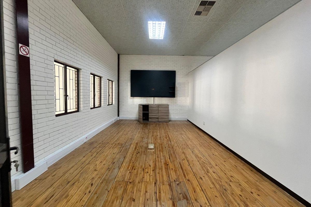 A spacious office area featuring timber flooring, exposed brick walls, and integrated ceiling lighting, providing a functional workspace with a neutral aesthetic.