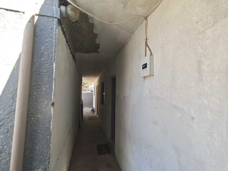 An exterior side passage or walkway featuring exposed electrical wiring, a distribution board, and unfinished wall surfaces requiring maintenance.