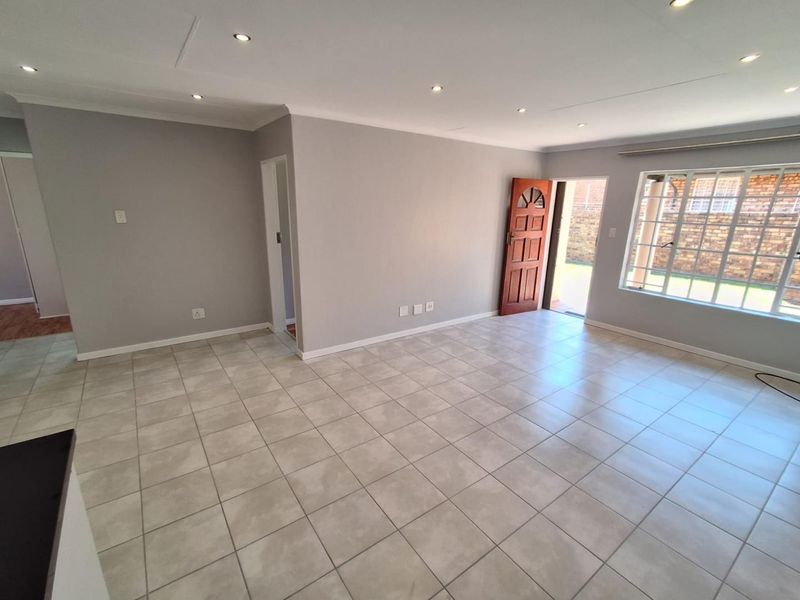Spacious, light-filled living area featuring neutral grey walls, tiled flooring, and recessed downlights, with direct access to the exterior.