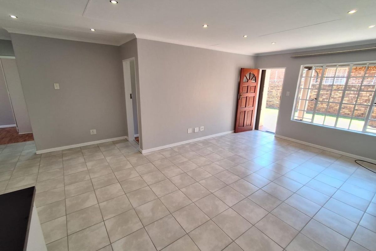 Spacious, light-filled living area featuring neutral grey walls, tiled flooring, and recessed downlights, with direct access to the exterior.