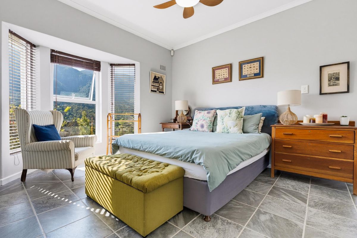 A well-lit bedroom featuring tiled flooring, a ceiling fan, and a bay window with mountain views.