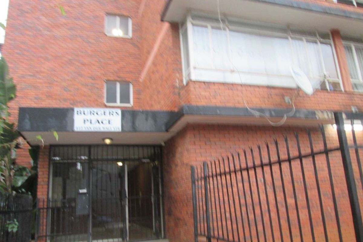 Front entrance view of the brick apartment building known as Burgers Place, featuring a secure gated entry and metal perimeter fencing.
