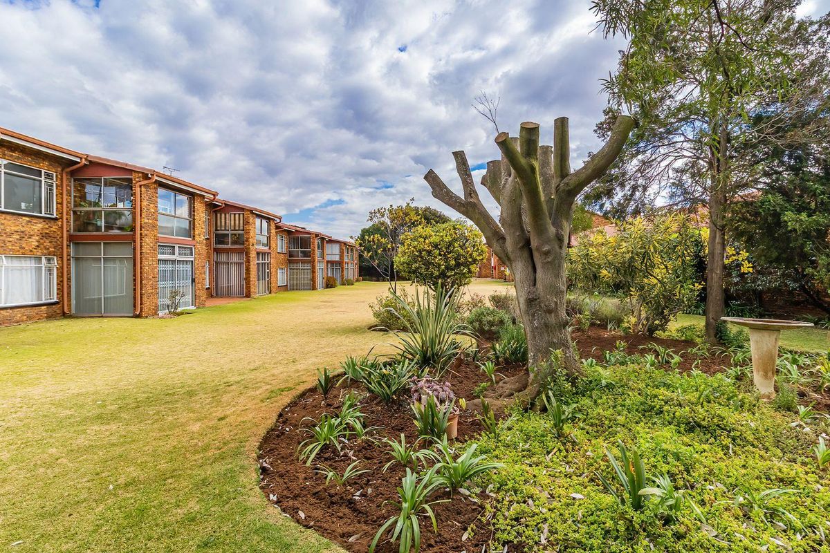 A view of the rear exterior of the townhouse complex, featuring a well-maintained lawn, landscaped garden beds, and face brick building facade.