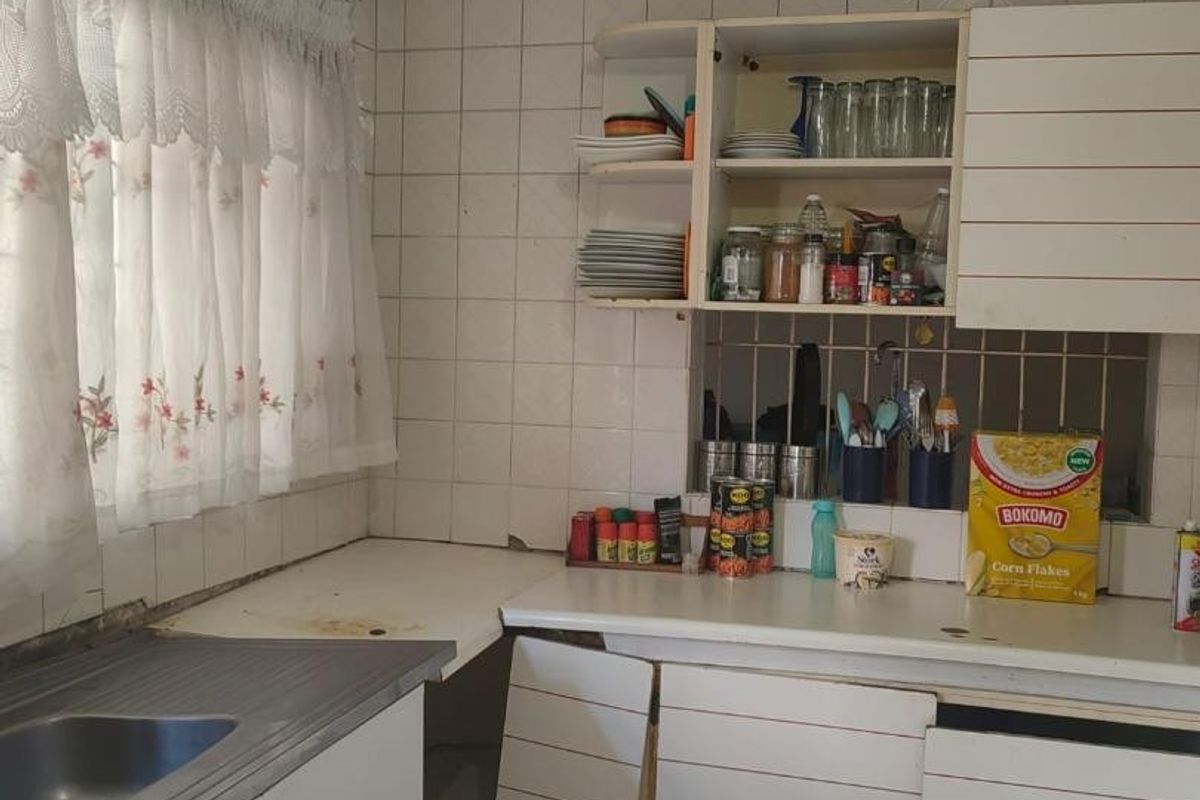 A dated kitchen featuring original cabinetry, tiled backsplash, and laminate countertops, currently requiring significant maintenance and cosmetic updates to improve functionality and aesthetic appeal.