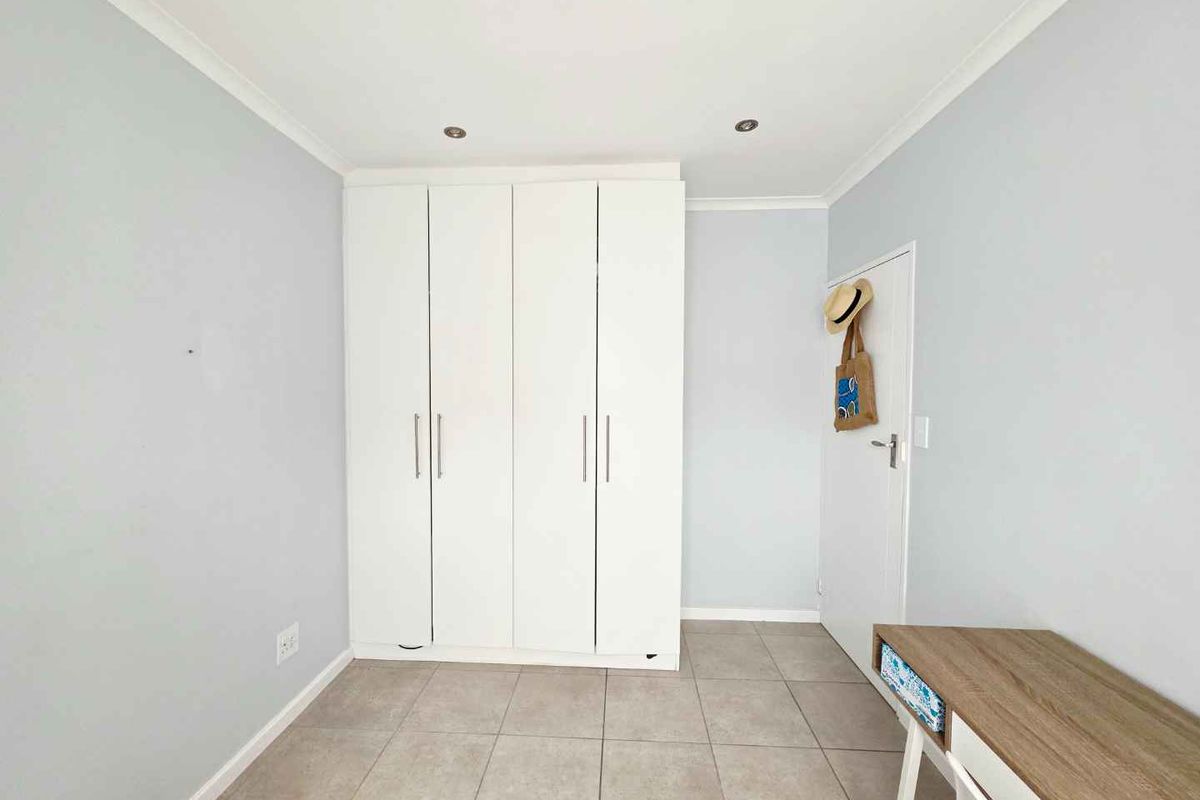 A clean bedroom featuring neutral tiled flooring, built-in white cabinetry, and recessed ceiling lighting.