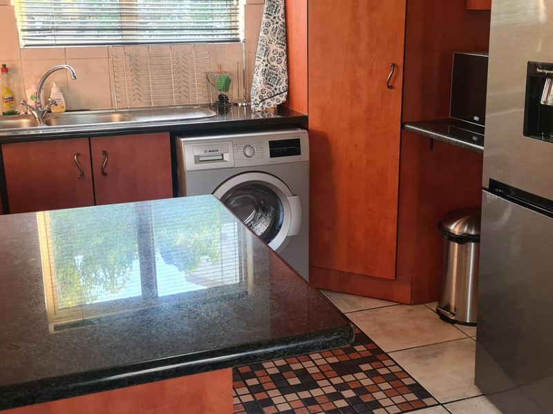 A functional kitchen featuring dark granite countertops, wood-finish cabinetry, tiled backsplash, and integrated laundry facilities with a stainless steel sink.