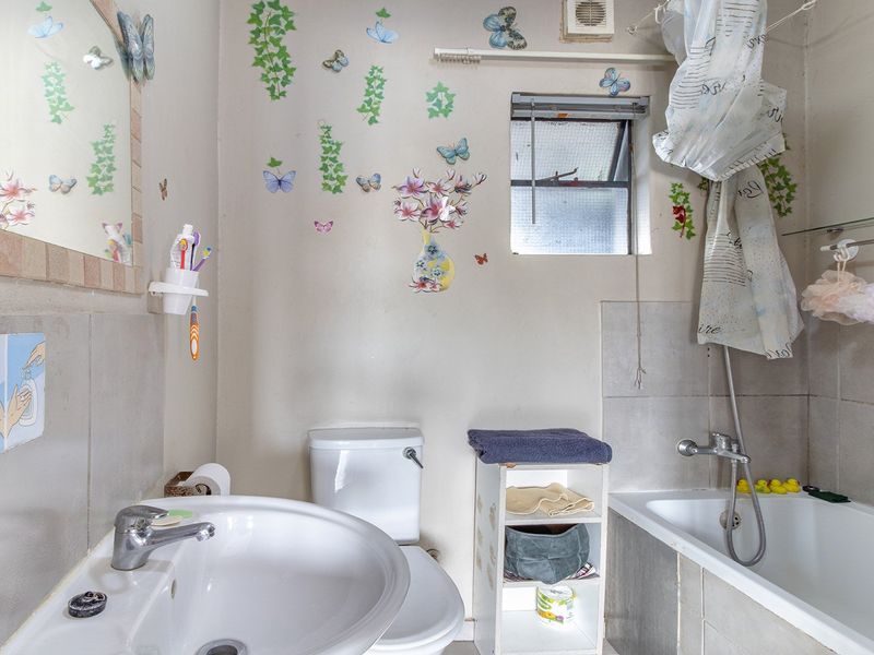 A functional bathroom featuring a pedestal basin, toilet, and bathtub with a tiled splashback and an integrated extractor fan.